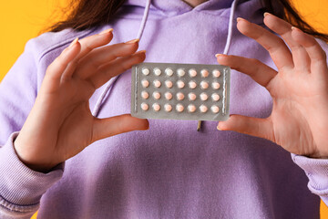 Young woman with contraceptive pills on orange background, closeup