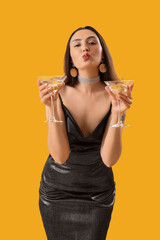 Beautiful woman with martini blowing kiss on orange background