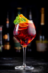 Red sangria summer alcoholic drink with red spanish wine, peach, plum, orange, lime and ice. Black bar counter background, steel bar tools and bottles