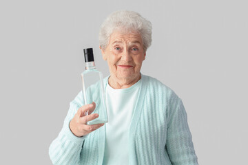 Senior woman with bottle of vodka on light background