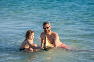 Obraz premium father and son beachside bonding. playing together dad and son. happy moments with father and son. Father son beach adventure playing with toy ship. Quality time in sea