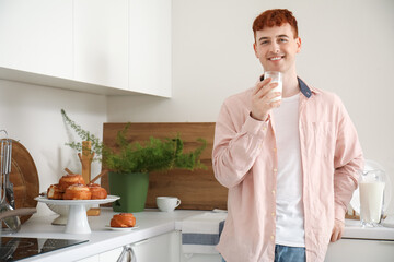Young redhead man with glass of milk in kitchen