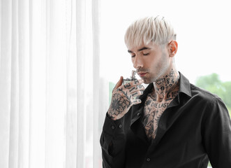 Tattooed young man with perfume near window at home