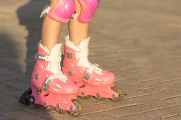Close up photo of little girl's legs on roller skates at a park. Cheerful preschool girl wearing...