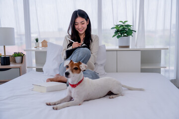 Asian Woman Working from the Comfort of Her Bedroom with Her Adorable Pet by Her Side