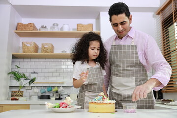 Happy lovely asian single dad and cute daughter in apron having fun with teaching and decorating homemade cake in the kitchen. Family lifestyle cooking with education concept.