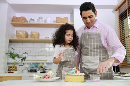 Happy Lovely Asian Single Dad And Cute Daughter In Apron Having Fun With Teaching And Decorating Homemade Cake In The Kitchen. Family Lifestyle Cooking With Education Concept.