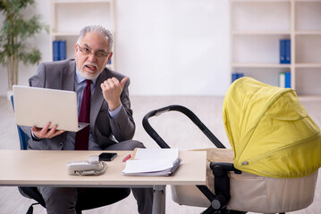Old male employee looking after new born at workplace
