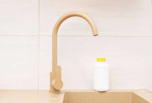 Pipe Drain Granules in White Plastic Bottle With Yellow Cap On Kitchen Sink In Cook Room. Clog Cleaner, Housework Help. Cleaning enzymes, Prevention of Blockages In Traps. Horizontal plane