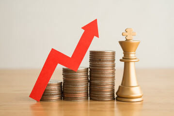 King chess and stacked coins as growth profit up graph with red arrow chart on wooden table with...