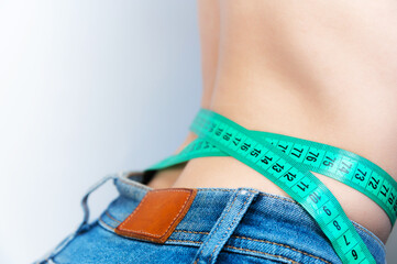 Close-up of a young beautiful woman measuring her waist. A woman measures the girth around her...
