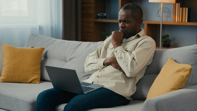 Thoughtful puzzled african american man businessman freelancer working on laptop at home couch think about solving business problem serious pensive male searching inspiration for new ideas thinking