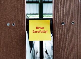 Yellow note stick  car park wall with text written DRIVE CAREFULLY,  to warn departing person to be...