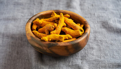 Fresh and dried turmeric roots in a wooden bowl. Grey textile background. Close up.