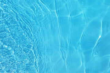 Blue water with ripples on the surface. Defocus blurred transparent blue colored clear calm water surface texture with splashes and bubbles. Water waves with shining pattern texture background.