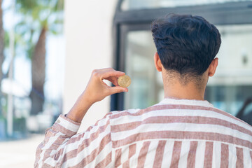 Handsome Arab man holding a Bitcoin at outdoors in back position