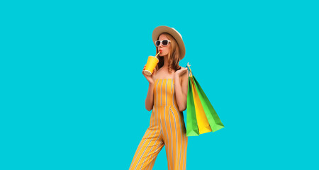 Beautiful young woman posing with shopping bags and drinks fresh juice wearing summer straw hat on blue background