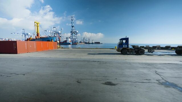 4K footage from moving vehicle on commercial port area with cranes, ship, trailers and containers in the background.   