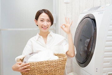 洗濯機の前で洗濯物を持ってOKポーズするミドルエイジの女性
