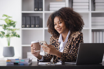 Young African American businesswoman working with smartphone and laptop at desk in office, business finance technology concept.