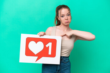 Young caucasian woman isolated on green background holding a placard with Like icon and pointing it