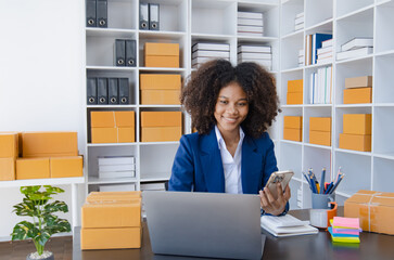 Happy African American businesswoman owner with a parcel box and checking orders from customers, online delivery service warehouse, sell products online concept.