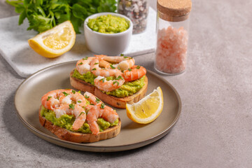 Appetizer toasted bruschetta with mashed avocado and shrimps on background. Healthy food concept with prawns.