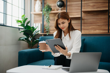 Young attractive Asian woman smiling thinking planning writing in notebook, tablet and laptop working from home at office .