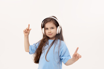 Happy smiling child girl enjoys listens to music in headphones over white background. Vivid and fun emotions, happy child with pleasure listens to songs in wireless headphones