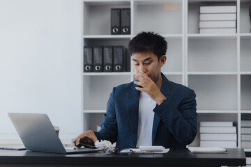 Asian businessman working online with laptop are stressed and tired from work sitting at desk in the office, feeling sick at work, stress from work.	