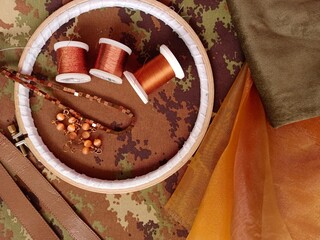Copper threads and beads inside an embroidery hoop. Background of orande tulle and camouflage fabric.
