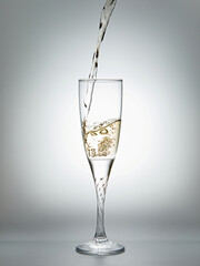 Pouring champagne into glass on gray background.