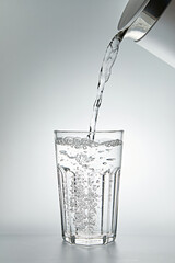 Pouring water into a glass on grey background