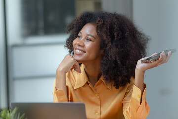 Happy young African American businesswoman using smartphone sitting at office desk. Happy woman and digital technology, woman using smartphone for video conference online with friends.