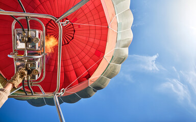 shot from below of a red hot air balloon with the burner lit and blue sky in the background