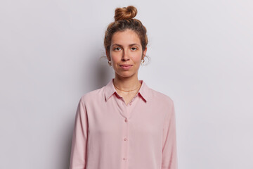 Professional studio portrait of young happy brunette beautiful pierced European lady isolated in centre on white background wearing pink blouse keeping hands down with bun. People emotions concept