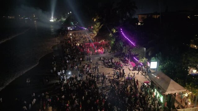 Mirissa, Sri Lanka,12.31.2022: beach nightclubs aerial view. Sea front cafes and restaurants colourful lights at night, crowd dances by sea at New Year celebration party down view from drone