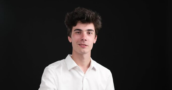 On a black background, a positive Caucasian man stands, radiating a cheerful and vibrant energy. He raises his index finger to his lips, gesturing the shh or tsk tsk sign.