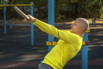 man trains with gymnastic rings on a street sports ground on a sunny day. Healthy lifestyle. Close-up