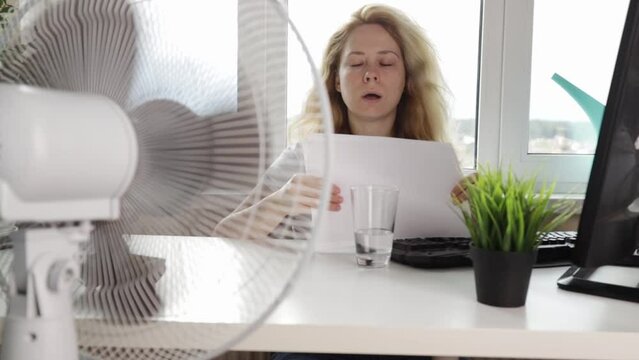 Woman using a fan to stay cool indoors, Preventing heatstroke, office worker in the heat at the workplace in the office