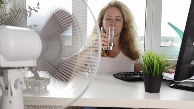 heat in the office,Woman blowing a fan to stay cool and comfortable, trying to cool down in a non-air-conditioned, office worker drinking water, Dehydration, heatstroke, summer heat
