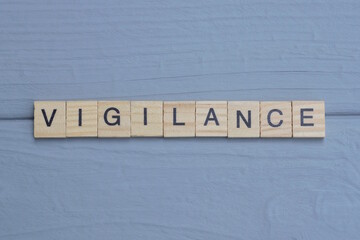 text the word vigilance from brown wooden small letters with black font on an gray table