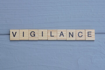 text the word vigilance from brown wooden small letters with black font on an gray table