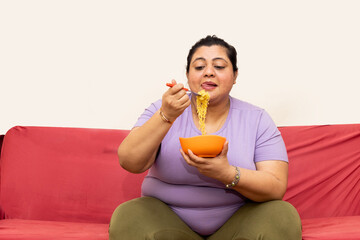 Asian indian fat woman having fun eating Noodles , she eats it with relish in at home. Fast food...