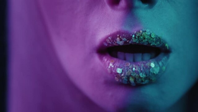 Close up the beautiful mouth of a girl. Beauty portrait of a face with lush lips of a woman, sexy kiss. Healthy female with bright plum lipstick, glitter, sequins on the skin. Neon light in the studio