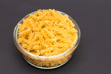 Uncooked Fusilli Pasta in Glass Jar on Black Background. Fat and Unhealthy Food. Classic Dry Spiral Macaroni. Italian Culture and Cuisine. Raw Pasta