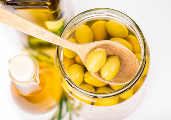 Close up green olives in a wooden spoon and a bottle of olive and
