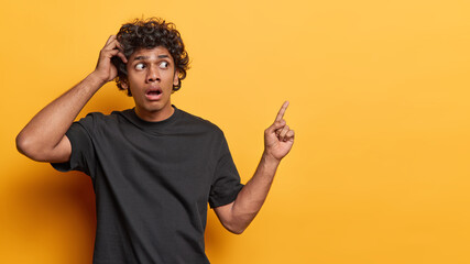 Horizontal studio shot of shocked young Hindu man with curly hair man gasping from amazement stares...
