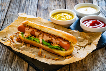 Hot dog bun with sausage and fresh vegetables on wooden table
