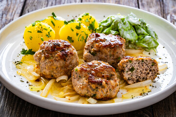 Seared pork meatballs with fried onion, boiled potatoes and lettuce in cream sauce on wooden table
